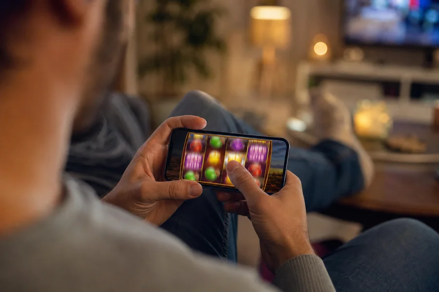 Thumb on smartphone playing a slot, cosy couch setting